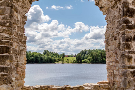 通过Koknese城堡的废墟观赏河岸上的乡村小屋，这是拉脱维亚领土上最大和最重要的中世纪城堡之一，现在部分被淹没了。