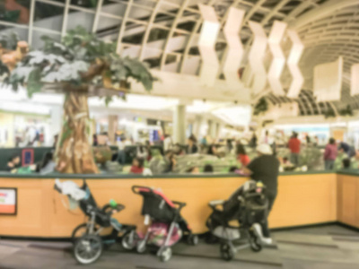 运动模糊了不同的孩子和父母在软玩设备室内操场的现代购物中心在美国。 外面一排婴儿车