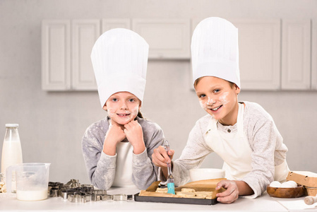 快乐的孩子们穿着围裙，在厨房的烤盘上刷着饼干