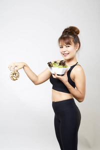 年轻女性瑜伽，在白色背景概念上持有带有垃圾食品的甜甜圈，健康食品