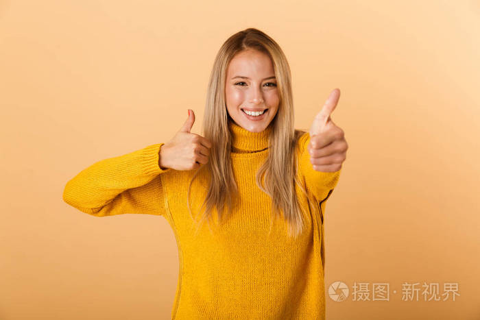 一位穿着毛衣的年轻女士的肖像，她站在黄色背景下，竖起大拇指