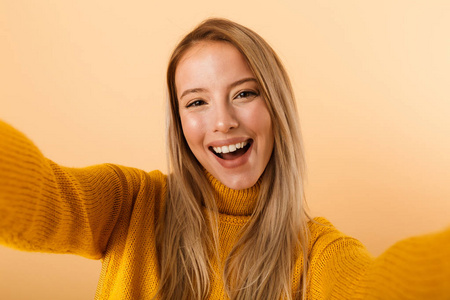 一位穿着毛衣的快乐年轻女子的肖像，站在黄色背景下，自拍