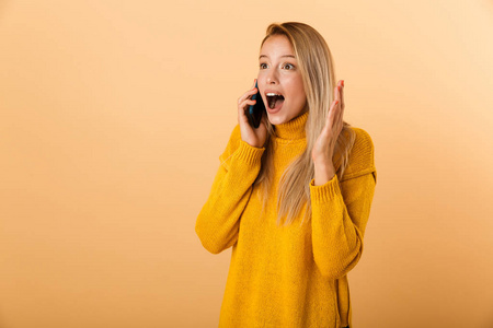 一位穿着毛衣站在黄色背景下在手机上聊天庆祝成功的年轻女子的肖像画