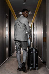 带行李走在酒店走廊的非裔美国商人的后景