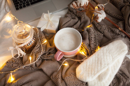 一杯热卡布奇诺在床上。舒适的装饰。早餐。木耳，格子，棉花，笔记本电脑，蜡烛..礼品盒和针织手套。圣诞灯。假日。