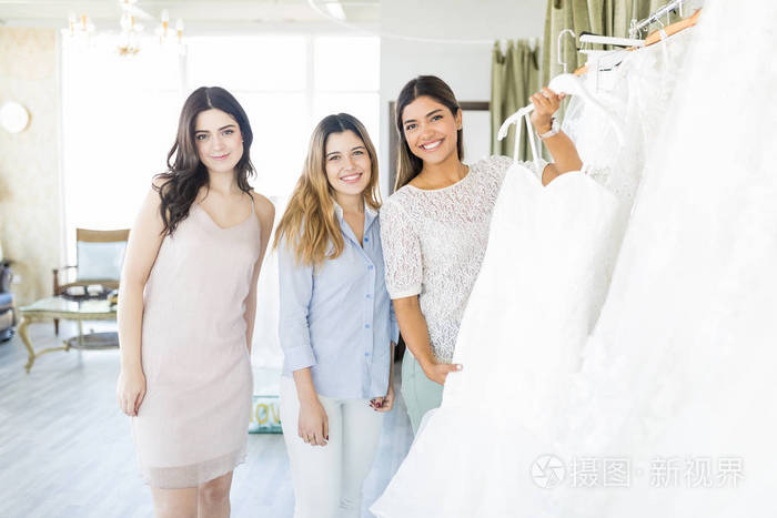 快乐的新娘在服装店和伴娘一起买婚纱