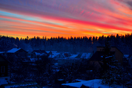 五彩缤纷的冬天日落覆盖着白雪覆盖的森林和村庄,雪中有房子.