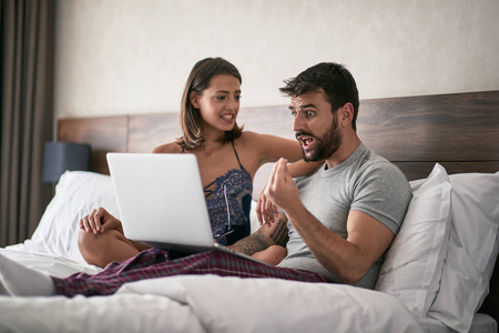 年轻人和女人在床上讨论笔记本电脑和上网。 现代生活方式概念