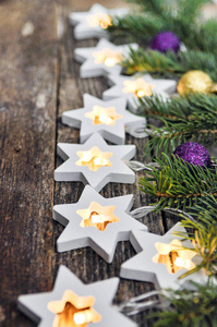 圣诞节边界舒适的温暖灯光，花环，星星和冷杉树枝，装饰着金色和紫色的球在乡村的木制背景上。 上面的风景。 手一伸。 复制空间