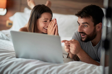 快乐的一对夫妇在家里的床上躺着一台笔记本电脑