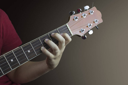 靠近一位年轻吉他手的左手，在一把吉他的脖子上。 在棕色背景上拍摄的照片。