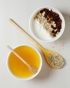 燕麦片加葡萄干和酸奶。 麦片在木勺里。 蜂蜜在白色的碗里。 平顶景观。 在白色的桌子上