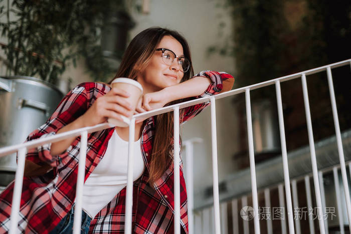 美丽的年轻女士与热饮靠在楼梯栏杆