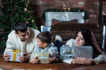 幸福的家庭躺在地板上，圣诞树背景上有礼品盒