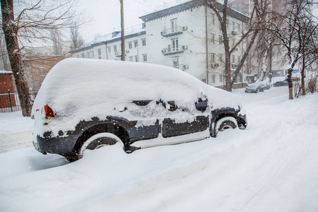 在停车场的冬季暴风雪中，车辆被雪覆盖。白雪覆盖的道路和城市的街道。