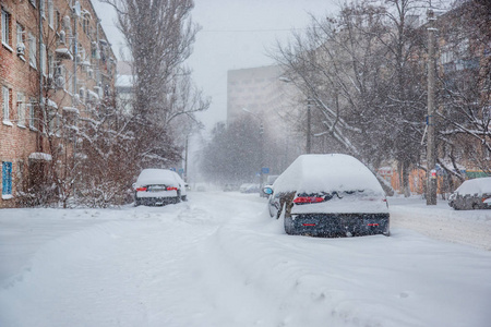 在停车场的冬季暴风雪中，车辆被雪覆盖。白雪覆盖的道路和城市的街道。