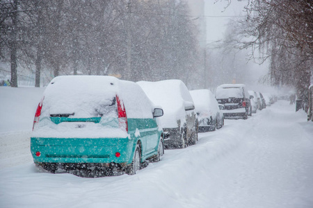 在停车场的冬季暴风雪中，车辆被雪覆盖。白雪覆盖的道路和城市的街道。