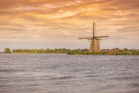 风景在美丽的橙色日落与云天和一个古老的荷兰传统风车位于鹿特丹附近的罗特梅伦湖。