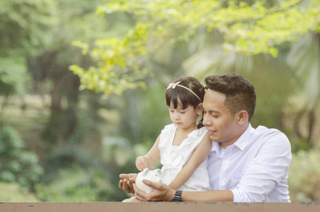 储蓄和教育观念年轻的父亲教她的女儿省钱。 坐在树下的长凳上