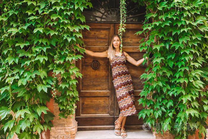 年轻女子在意大利老镇上摆姿势背景是绿色藤蔓和木门