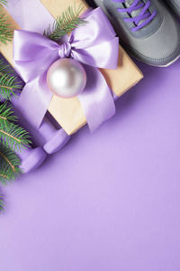 圣诞运动平躺构图灰色鞋紫色哑铃工艺礼品盒与紫丁香蝴蝶结云杉树枝在紫罗兰背景。 顶部视图水平方向。