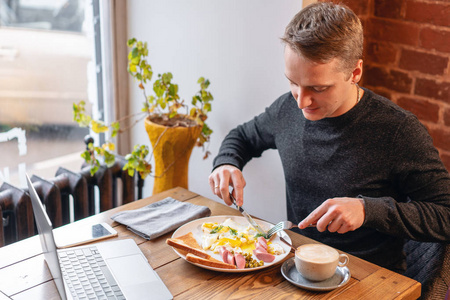 手里拿着刀叉.工作中吃饭的概念.笔记本电脑和餐单上的早餐.