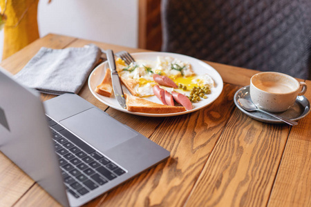 工作中吃饭的概念。笔记本电脑和餐单上的早餐。美式早餐, 包括煎蛋香肠青豆和吐司。健康早晨的概念