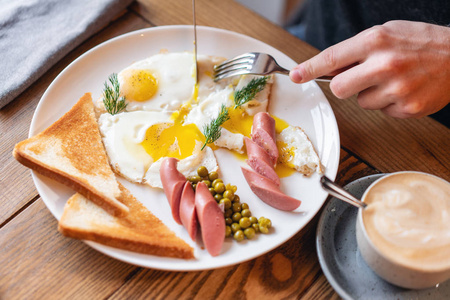 男人吃东西。手里拿着刀叉。在桌子上吃早餐。美式早餐, 包括煎蛋香肠青豆和吐司。健康早晨的概念