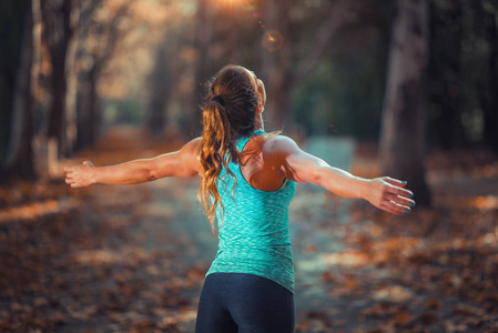 女人在公共公园秋天在户外锻炼。 举起手臂站立。