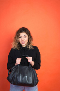 购物摘要漂亮的女孩带着黑色的袋子，背景是橙色的
