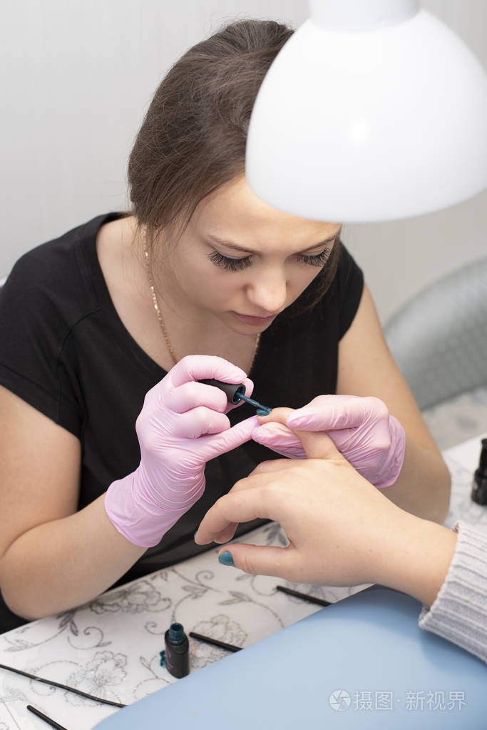 在美甲沙龙里, 戴手套的美甲师用刷子用绿色指甲油覆盖着客户的指甲