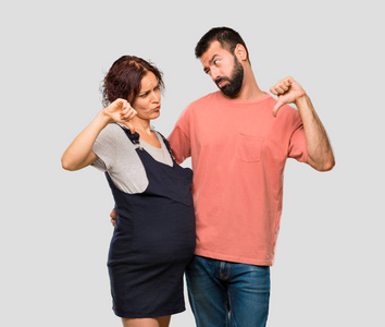 夫妇怀孕妇女显示拇指向下标志，阴性表达在孤立的灰色背景