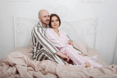 年轻漂亮的女人和一个穿睡衣的秃头男人抱着枕头和粉红色的床上用品在