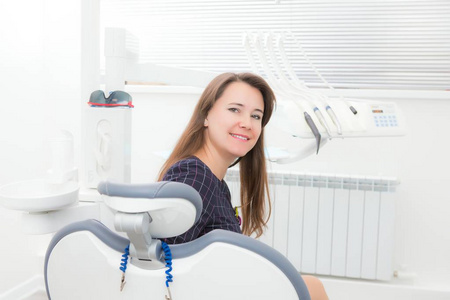 年轻的女病人坐在牙科办公室的椅子上准备牙科检查看着相机