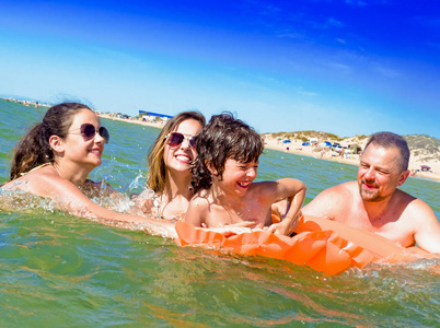 幸福的家庭四在海边度假。幸福的家庭与黄色床垫沐浴在海里。快乐的爸爸妈妈和两个孩子在水中玩耍