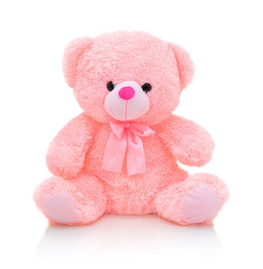 可爱的粉红色熊娃娃与蝴蝶结隔离在白色背景与阴影反射。 好玩的亮粉色熊坐在白色的衬垫上。 泰迪熊毛绒填充木偶与丝带在白色背景。