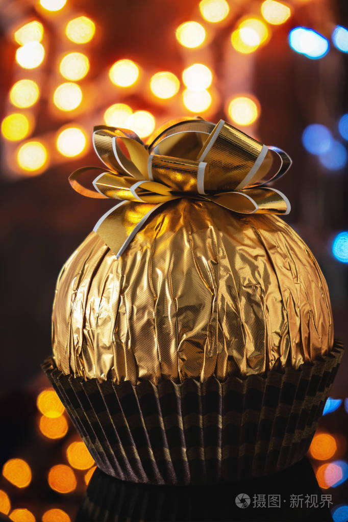 金色包装的大巧克力糖果和节日蝴蝶结礼物背景灯关闭