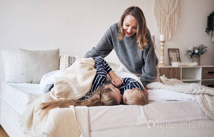 妈妈照顾. 年轻的母亲在卧室里用毯子覆盖孩子们. 兄妹拥抱睡在床上.