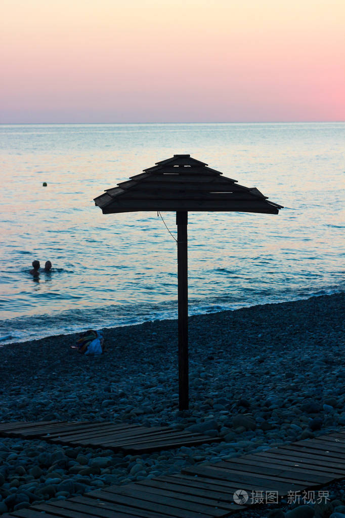 傍晚的海滩人们在海中游泳日落在海上粉红的天空遮阳的木伞在海滩上