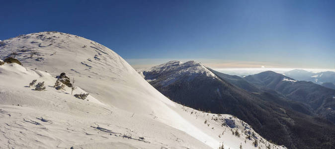 美丽的冬季景观。 陡峭的山坡与白色的深雪遥远的木本山脉全景延伸到地平线和明亮的阳光照射在蓝天复制空间背景。