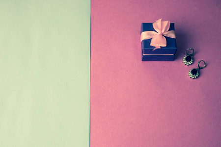 美容盒, 节日美丽的礼品盒与一个弓与银色耳环与宝石在粉红色紫色的背景。平躺着。顶视图