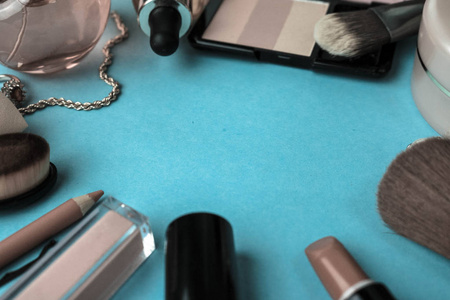 框架从一套女性化妆品从口红, 荧光笔, 铅笔的嘴唇, 刷子, 刷子, 香水, 粉末, 饰品上的蓝色背景。美容盒平躺。顶视图