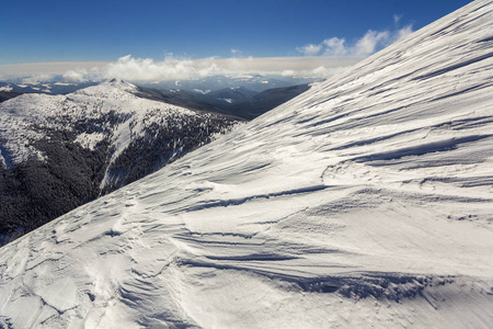 美丽的冬季景观。 陡峭的山坡与白色的深雪遥远的木本山脉全景延伸到地平线和明亮的阳光照射在蓝天复制空间背景。