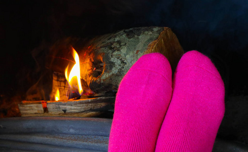 壁炉前燃烧的木头,穿着粉红色袜子的女性脚暖和起来.