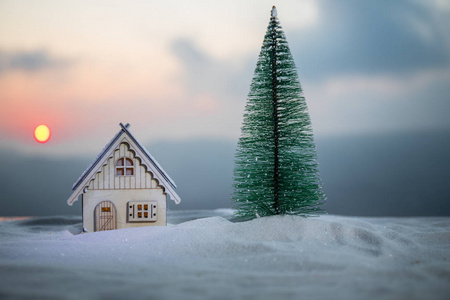 圣诞节和新年微型房子在雪地里的阳光。 带着树在雪地上的小玩具屋。 节日背景。 圣诞装饰品。 节日和庆祝概念。
