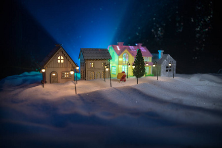 小装饰可爱的小房子在夜间雪在冬季圣诞节和新年微型房子在雪在夜间与杉树。 假日概念。 选择性聚焦