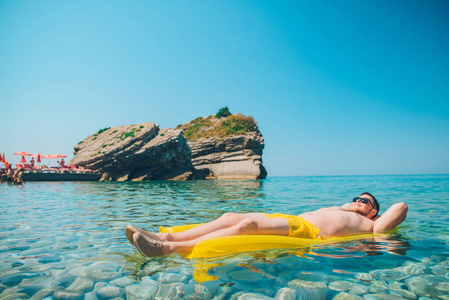 年轻人在黄色充气床垫在透明的水中。 暑假概念