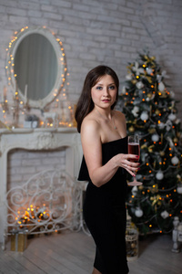 一位身穿黑色连衣裙的美女，手里拿着一杯香槟，摆在圣诞树的背景上