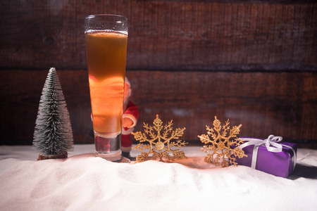 带有圣诞装饰的啤酒杯。 玻璃轻啤酒与泡沫在雪与创造性的新年假期艺术作品。 复制空间