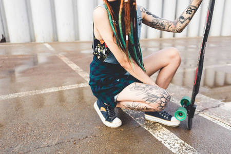 有纹身和长发绺的年轻女孩坐在混凝土结构的背景长板